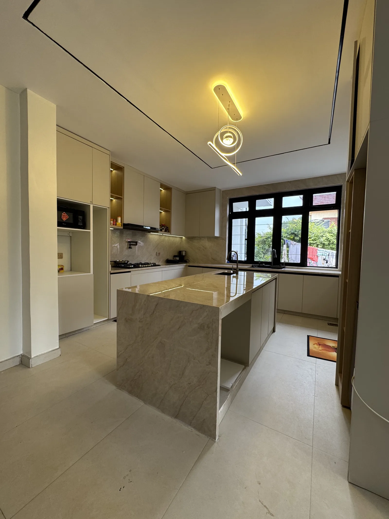 A stone kitchen island under pendant lighting, with a full run of cabinetry behind it