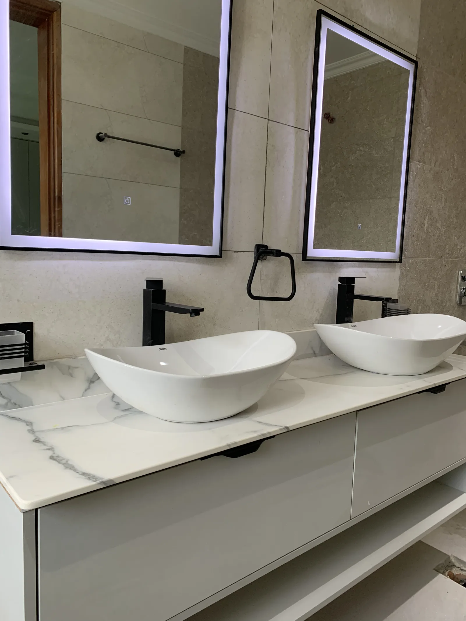 A double vanity counter in veined stone, with two vessel basins under backlit mirrors